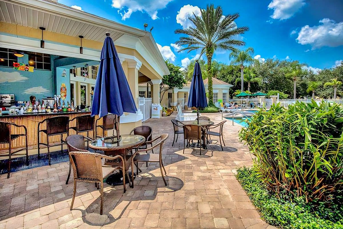 Poolside bar with umbrellas and wicker chairs, next to a pool surrounded by palm trees at Windsor Palms Resort.